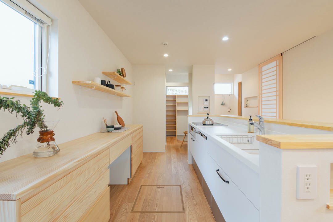 木の温もりと白を基調とした、岡崎市の注文住宅の美しいキッチン。広い作業カウンターの奥には大容量のパントリーが続き、料理から片付けまでがスムーズな家事ラク動線を実現。