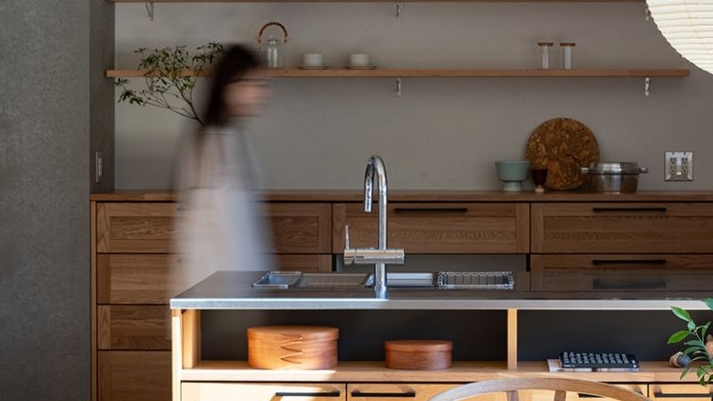 くらはし建築の施工事例。木の温もりとステンレスの天板を組み合わせたウッドワンのキッチン。塗り壁やオープン棚がジャパンディな雰囲気を演出し、人の気配が暮らしの豊かさを感じさせる一枚。