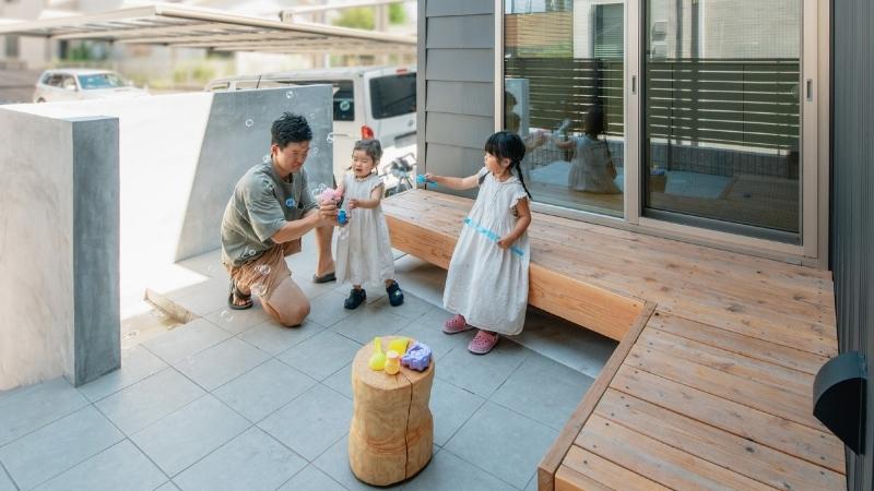 東向きの土地のメリットを最大限に活かした、岡崎市の注文住宅の庭。夏の午後の心地よい日陰で、ウッドデッキとタイルテラスでお子様と遊ぶオーナー様ご家族の幸せな日常。