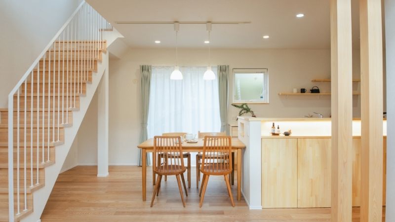 "大通り沿いの注文住宅の、明るく落ち着いたダイニング空間。吹き抜けを通して2階から降り注ぐ光が、1階のリビングダイニングを優しく照らす様子。