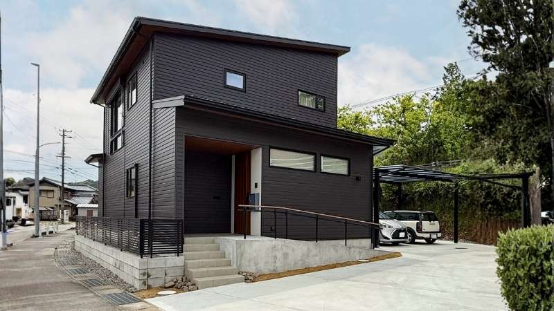 岡崎市の大通り沿いに建つ、黒いガルバリウム鋼板のモダンな注文住宅。1階の窓を最小限にしプライバシーを確保しつつ、2階の高窓で採光する設計思想が外観にも表れている。