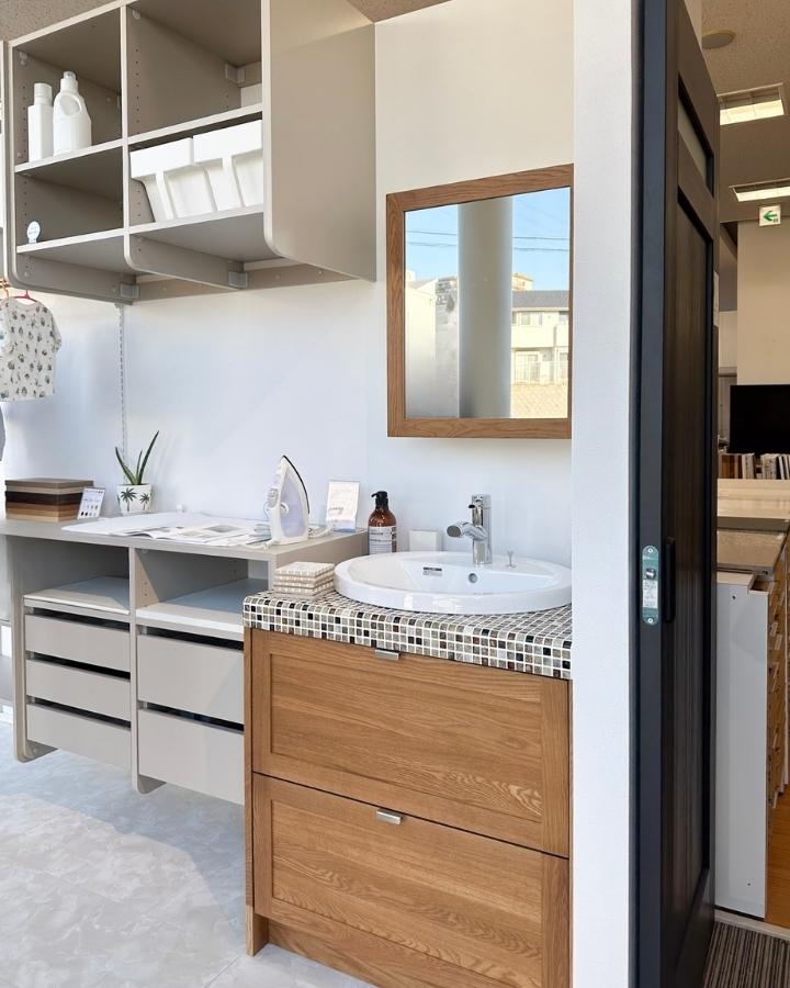 ウッドワンの洗面化粧台とランドリー収納。タイルと無垢の木がおしゃれな洗面台に白い洗面ボウル、その上には木枠の鏡。左には棚と引き出しの収納。ナチュラルなインテリアにピッタリです。