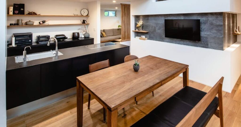 くらはし建築のモデルハウスのLDK。高い吹き抜けには木の梁が渡され、黒いアイランドキッチンと木のダイニングテーブルが置かれている。