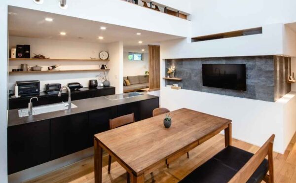 くらはし建築のモデルハウスのLDK。高い吹き抜けには木の梁が渡され、黒いアイランドキッチンと木のダイニングテーブルが置かれている。