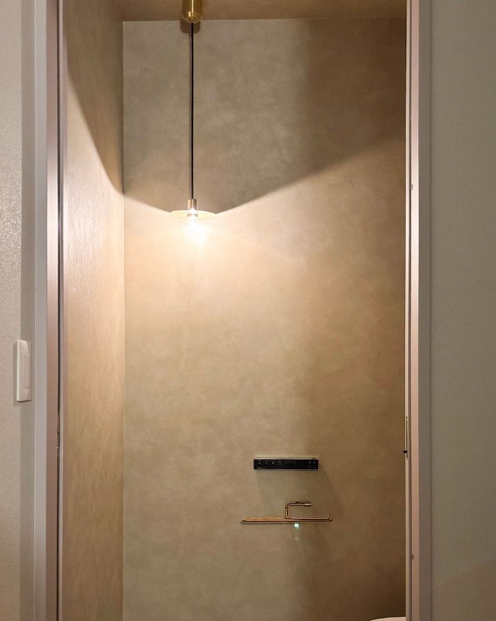 真鍮のペンダントライトとグレーの壁が美しいトイレ ホテルライクな空間