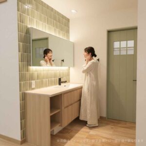 岡崎市寿町の注文住宅のイメージ画像。モスグリーンのタイルと間接照明がおしゃれな造作洗面台。忙しい朝も気分が上がる大人かわいいデザイン。