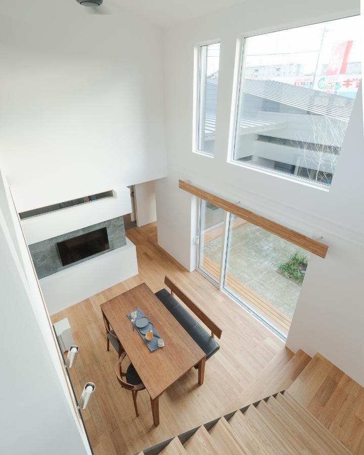 吹き抜けの階段から見下ろす、大きな窓から庭の緑がのぞく明るく開放的なダイニング。