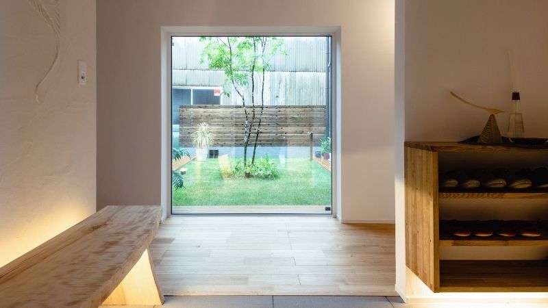 玄関ホールから大きな窓越しに眺める、中庭の美しい木々と柔らかな光が差し込む空間。